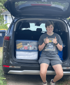 Felix sitting in the trunk of a car, next to some bins and boxes.