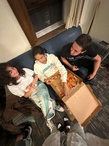 Defne and two friends sit on a couch, enjoying a pizza