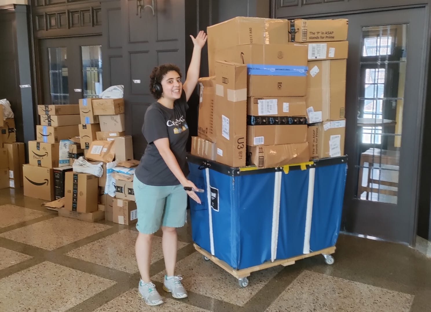 A [short] student stands next to a big pile of boxes.