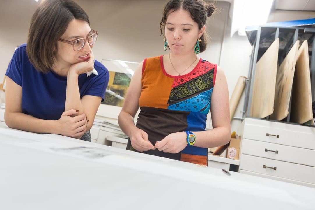 A professor and a student stare at a printmaking project on the desk.