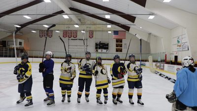 6 hockey players in Carleton College gear lifting their sticks in the air and cheering