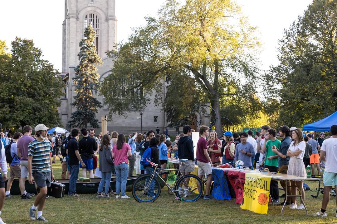 On a sunny day, students walk around a field to different club tables.