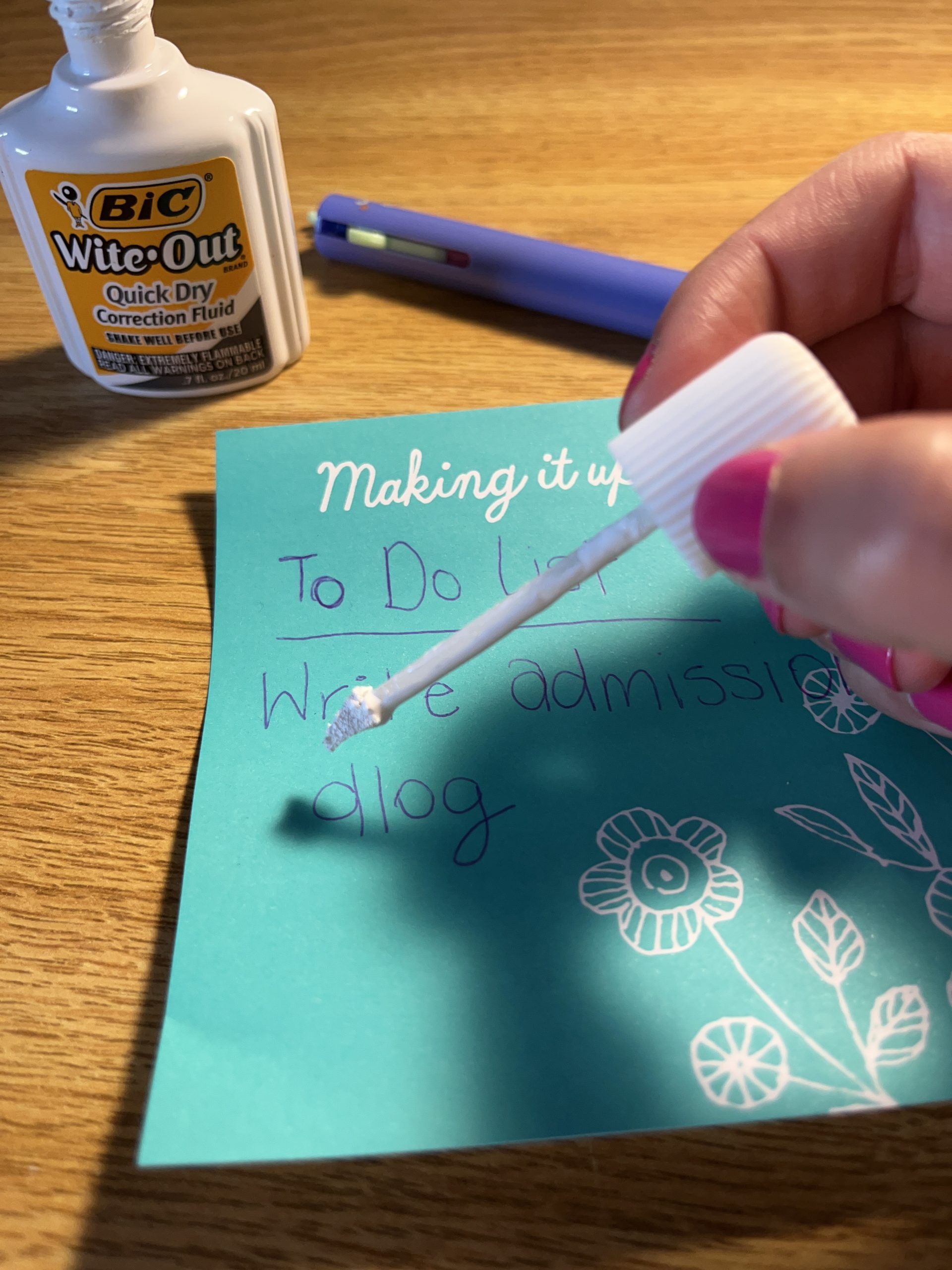 Lexi applies white correction fluid to a teal-colored note