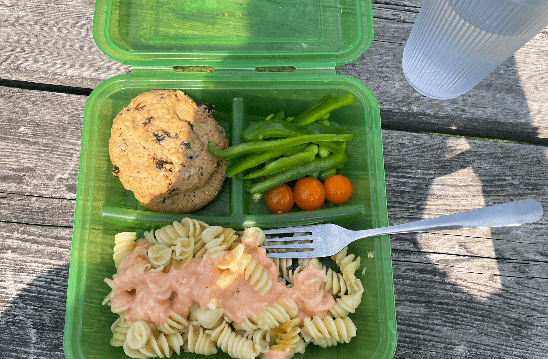 A green box filled with cookies, pasta, green peppers, and tomatoes sitting on a picnic table.