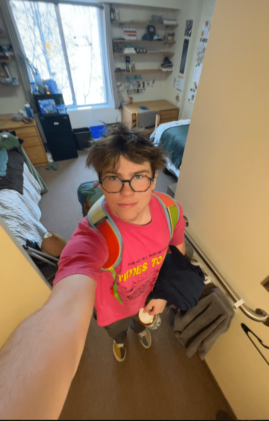 Felix stands in the hallway of his dorm room wearing a backpack