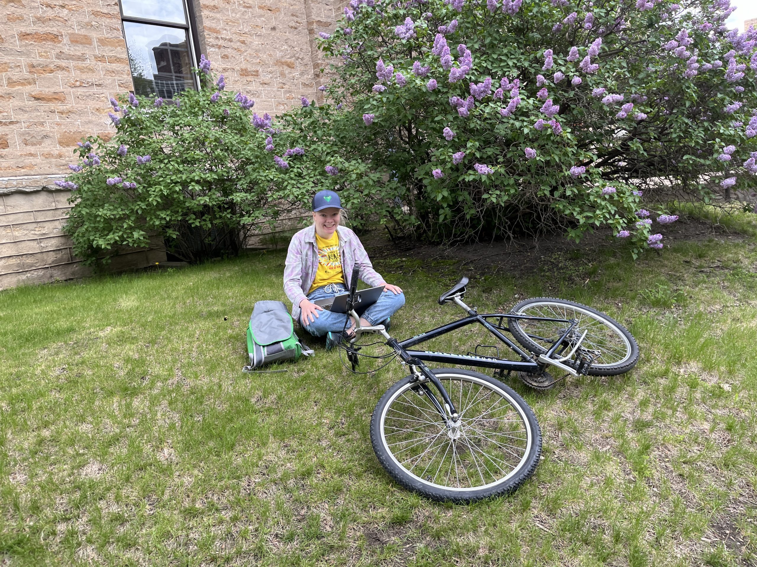 Klara sits on a grassy hill with her laptop and bicycle