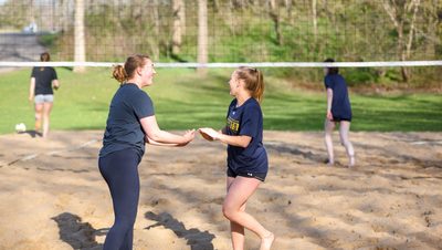 Two girls high fiving on a beach volleyball court