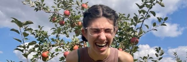 Annie laughing and hold apples in front of an apple tree