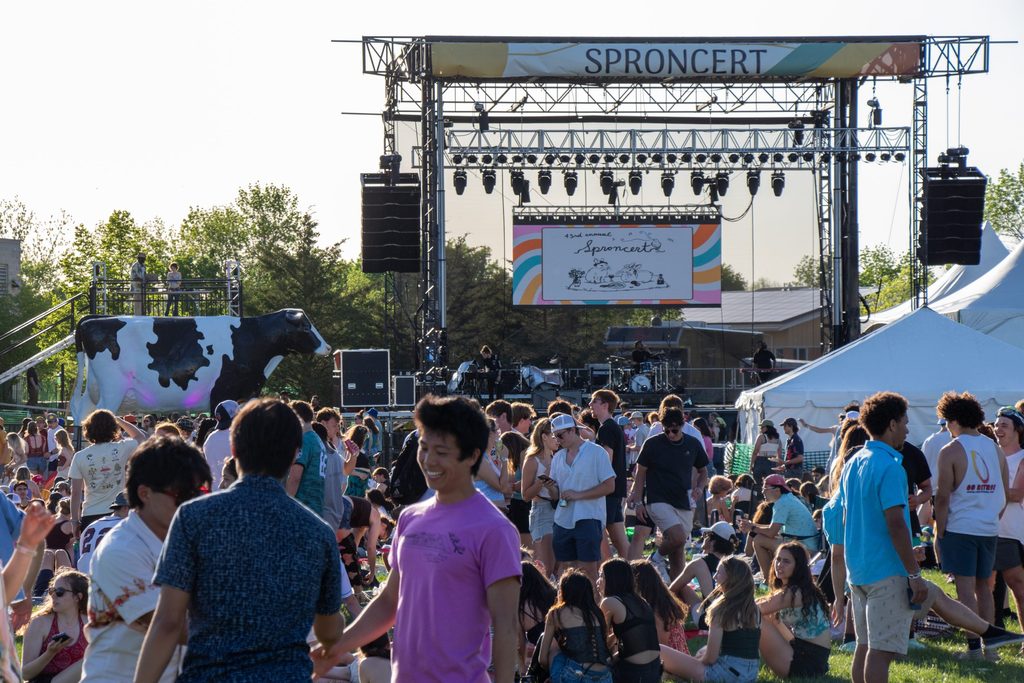 an expansive concert scene. students fill the grassy area and a large stage with a jumbotron can be seen in the back