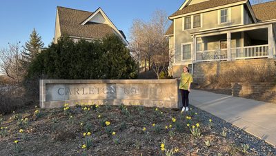 A girl smiling next the Carleton sign