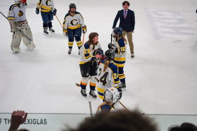 Carleton women's ice hockey player with helmet off laughing and talking to other players