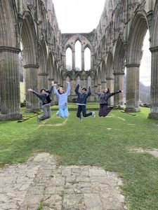 A group of students jumping at a ruined Abbey