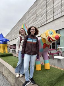 Two girls smiling next to a lambanana (a mix of lamb and banana)