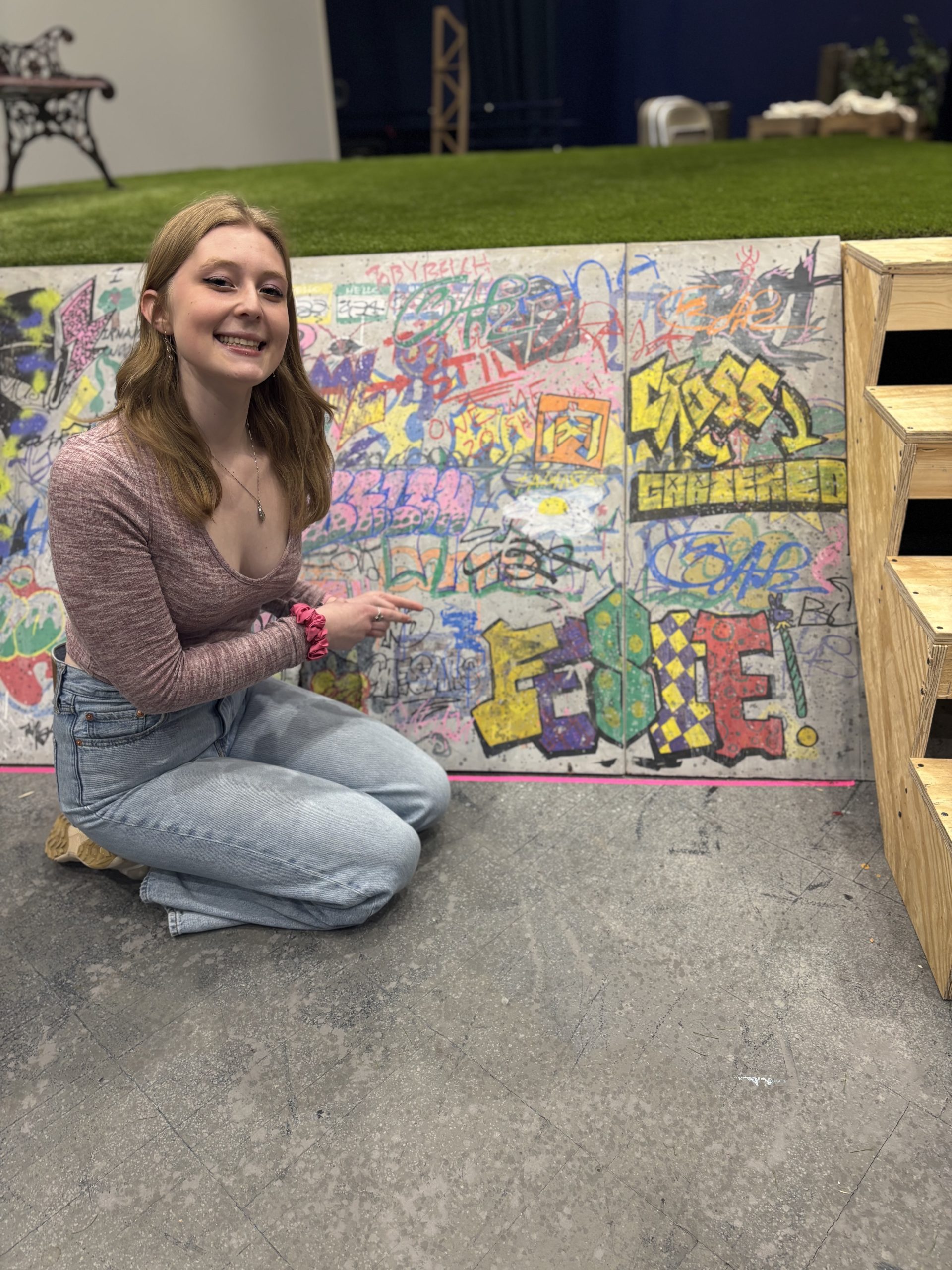 a girl posing in front of stage graffiti saying "Feste"