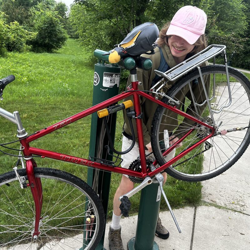 A Carleton student in a pink hat works on their bike at a free bike work station