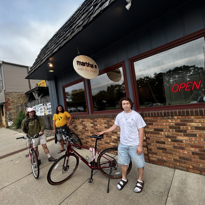 3 students with bikes standing in front of a bakery