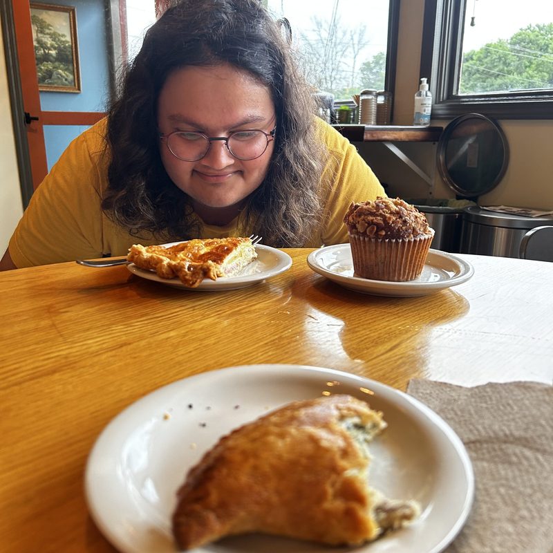A student with long hair looks down at a quiche with a muffin and a scone in the background