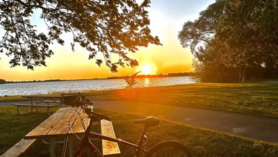 a maroon bike leaning on a table in front of a lake at sunset
