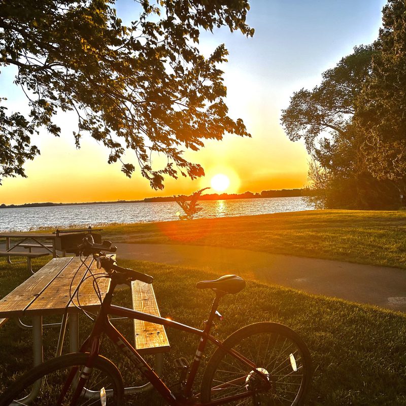 a maroon bike leaning on a table in front of a lake at sunset
