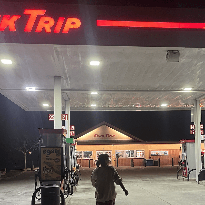 A student with long hair walking in front of a gas station