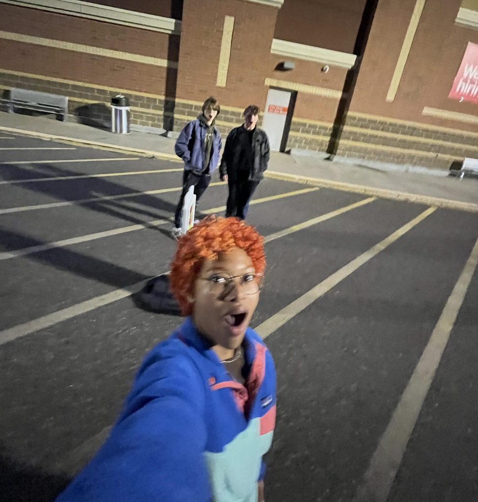 A student takes a selfie with two other students in the background.