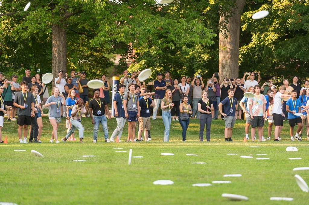 A group of first-year students throw frisbees on a grassy field. 
