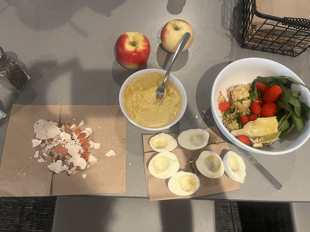 A bowl of salad, two apples, and boiled eggs ready for the deviled egg filling sit on a table