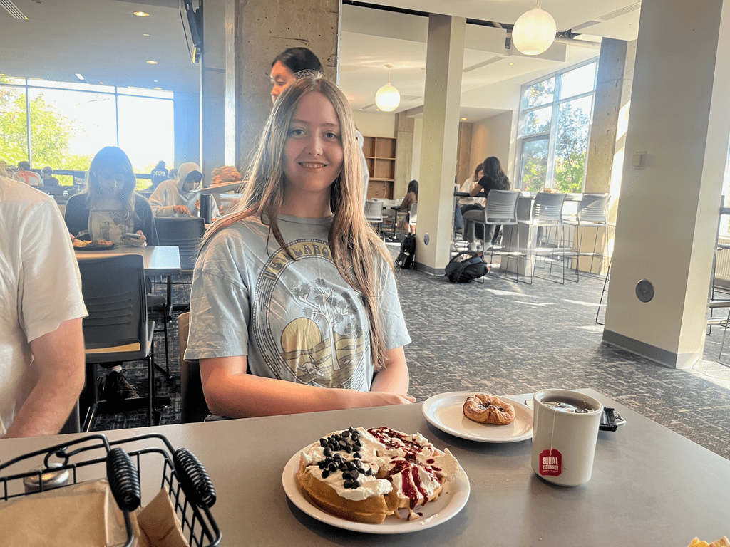 A student sits proudly in front of a waffle topped with whipped cream.