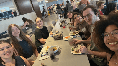 A student takes a selfie at a dinner table full of friends