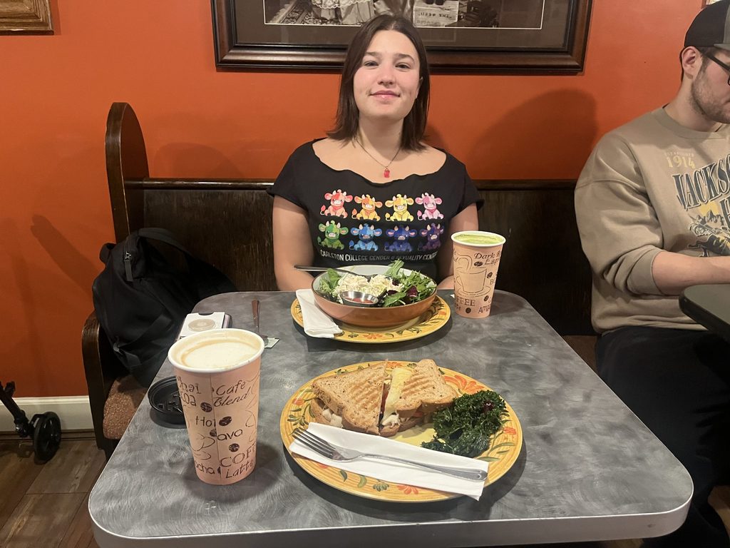 A student sits at a coffee shop in front of a salad and hot drink.