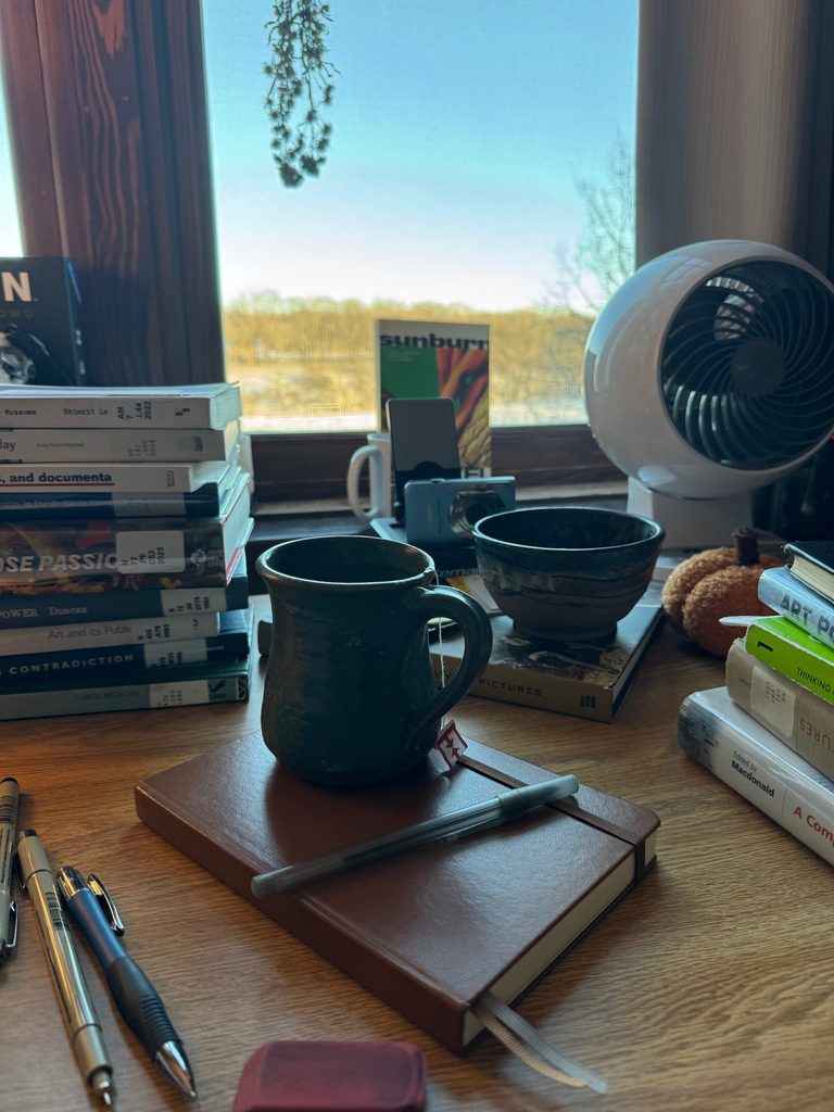 A mug, notebook, and other miscellaneous things on a desk.