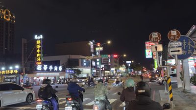 A nighttime picture with motorcyclists and cars.