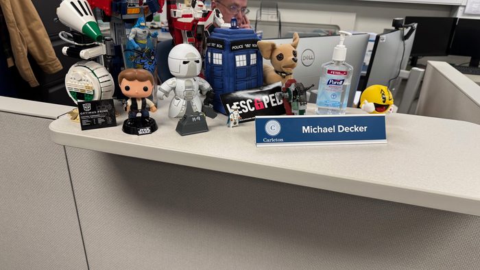 A desk shelf with a bunch of nerdy trinkets and a name plate that reads Michael Decker