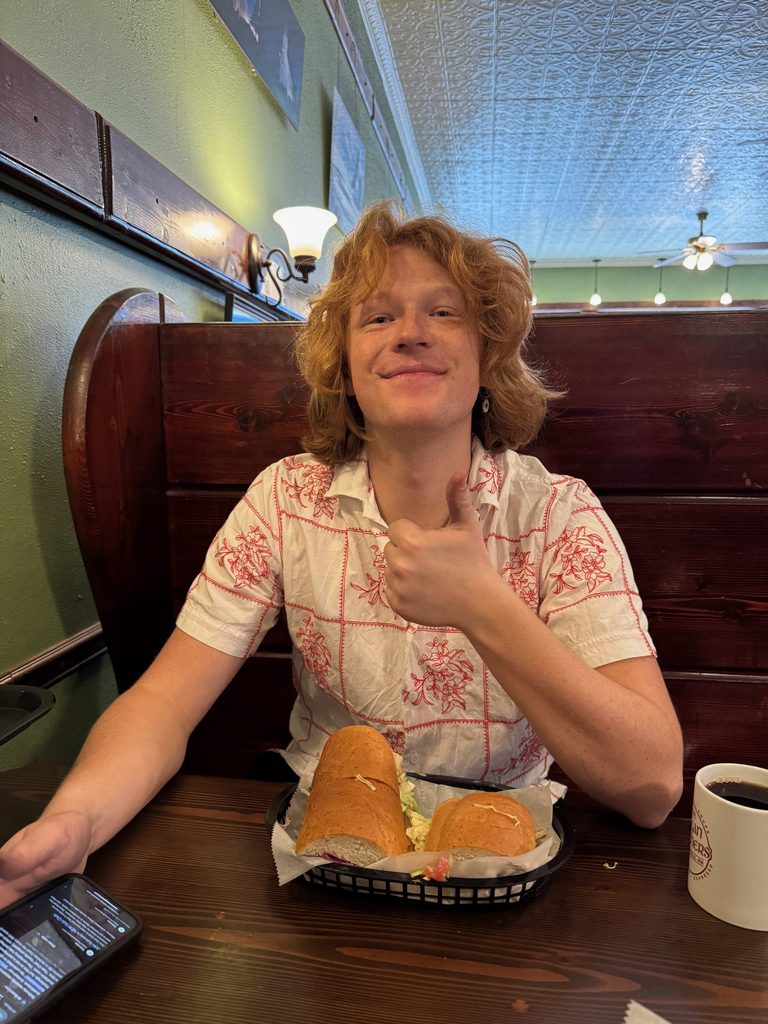 Schuylar at a booth in a restaurant giving the camera a smile and a thumbs up
