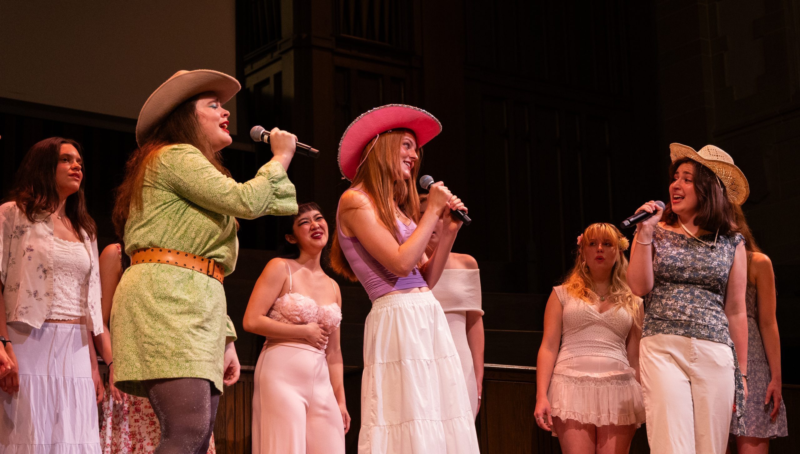 Three girls singing into microphones together wearing cowboy hats and florals.