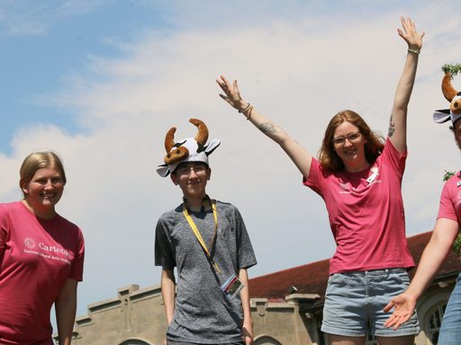 A Summer Carl stands and smiles, surrounded by Carleton summer student staff members.