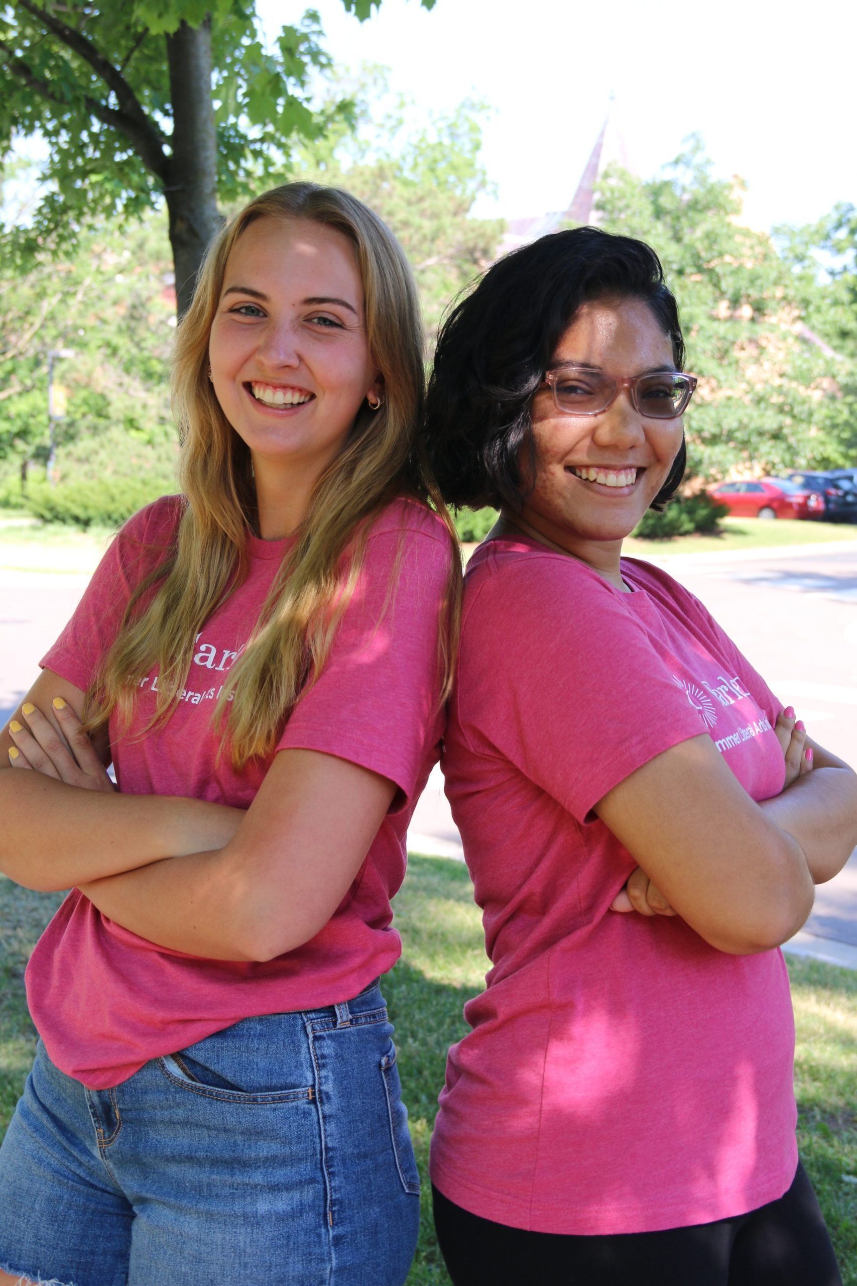 Two students wearing SLAI shirts standing back to back with their arms crossed, smiling. 
