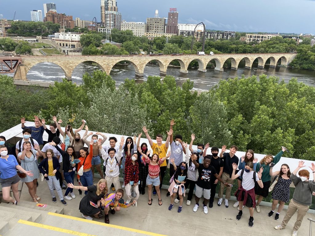 A group of students gathered on a balcony overlooking the Minneapolis skyline and Stone Arch Bridge. 