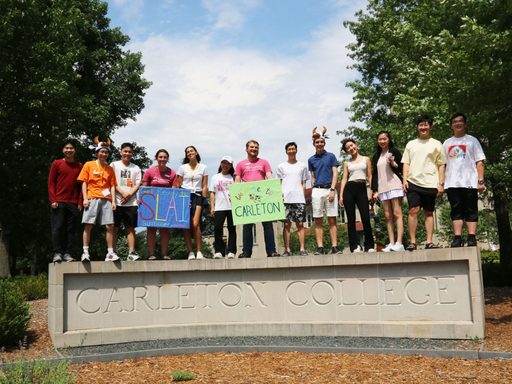 13 students welcoming summer Carls atop the Carleton College sign.