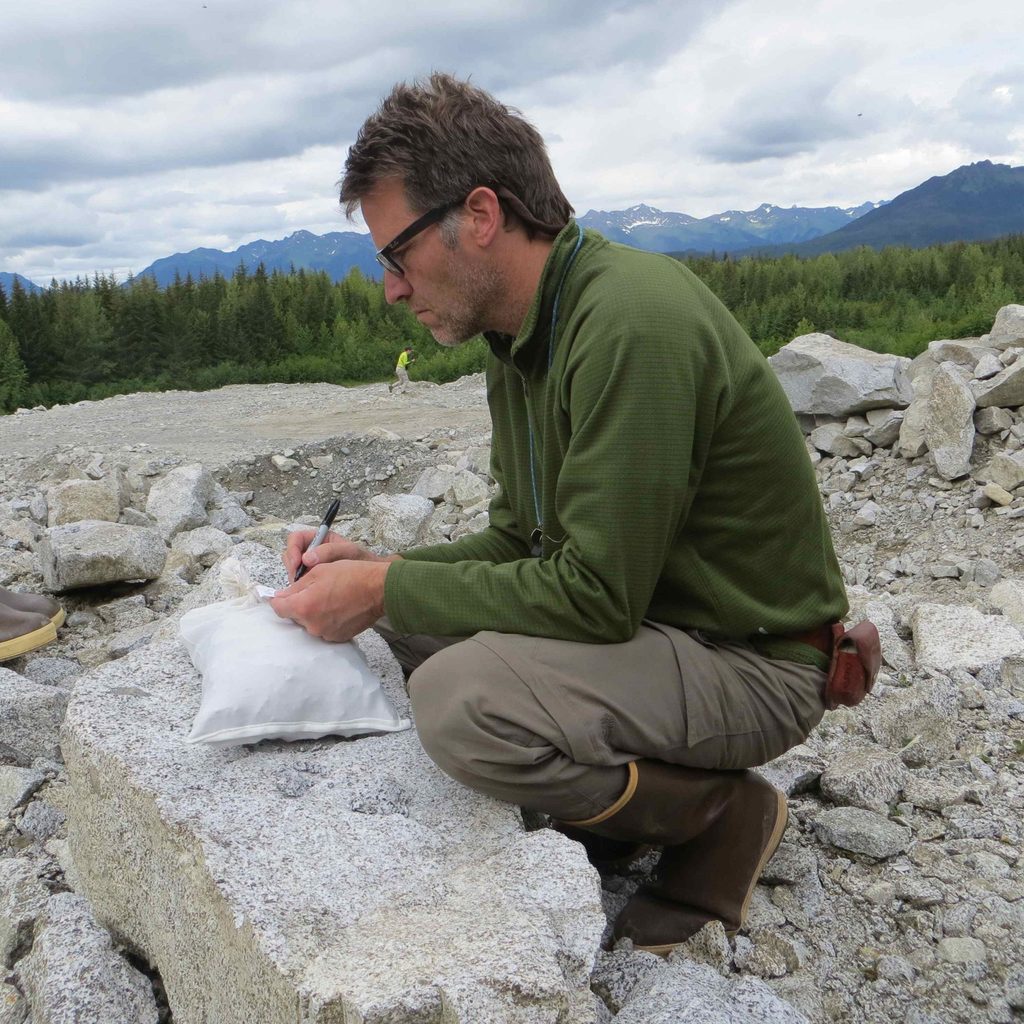 Professor Cam Davidson crouching over a big piece of granite.