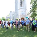A crowd of teachers searching for their workshop consultants, who are holding blue signs, in front of Carleton's chapel.