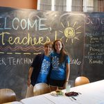 Two Carleton staff members smile in front of a chalkboard that says Welcome, Teachers! Summer Teaching 2016. and a Schedule of Events.
