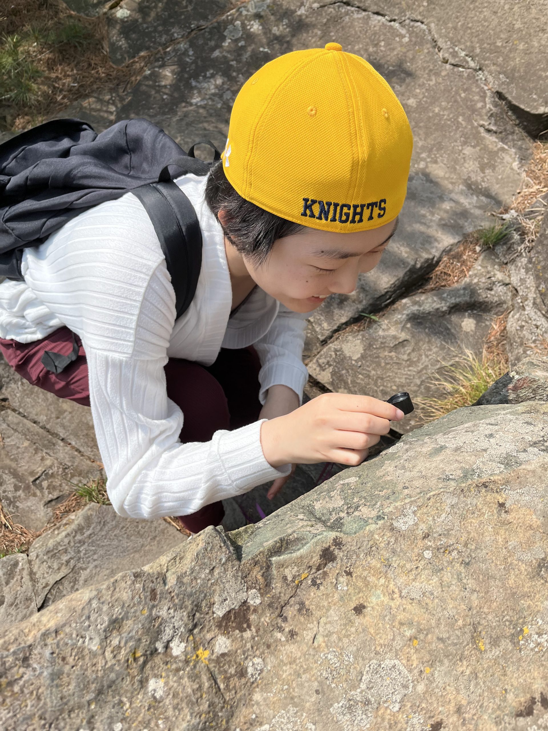 A student wearing a yellow "Knights" hat looks at a rock.