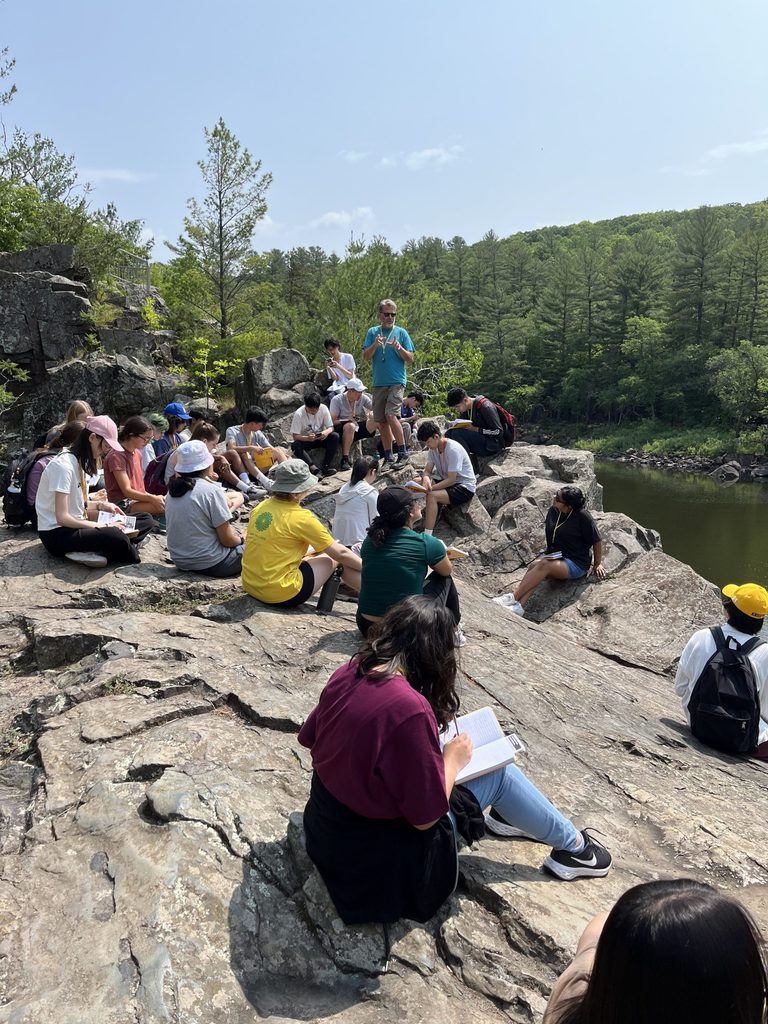 A group students sit on a rocky cliff with a professor.
