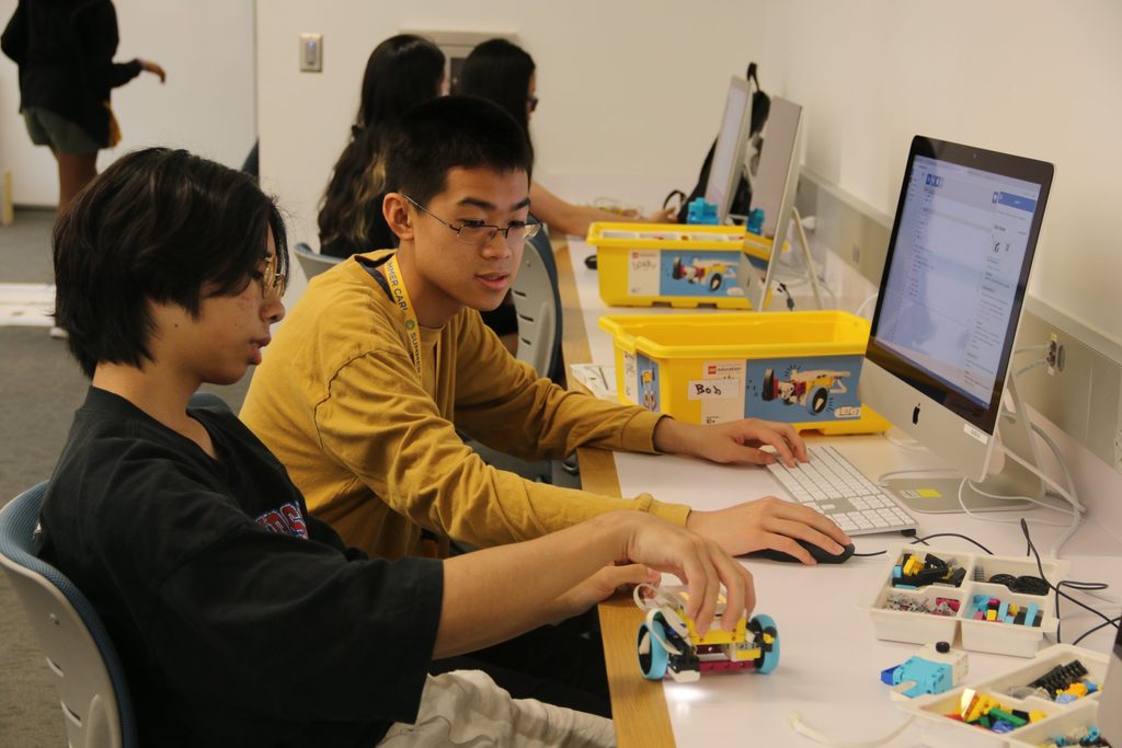 Two students working with a computer and a robot in a computer lab. 