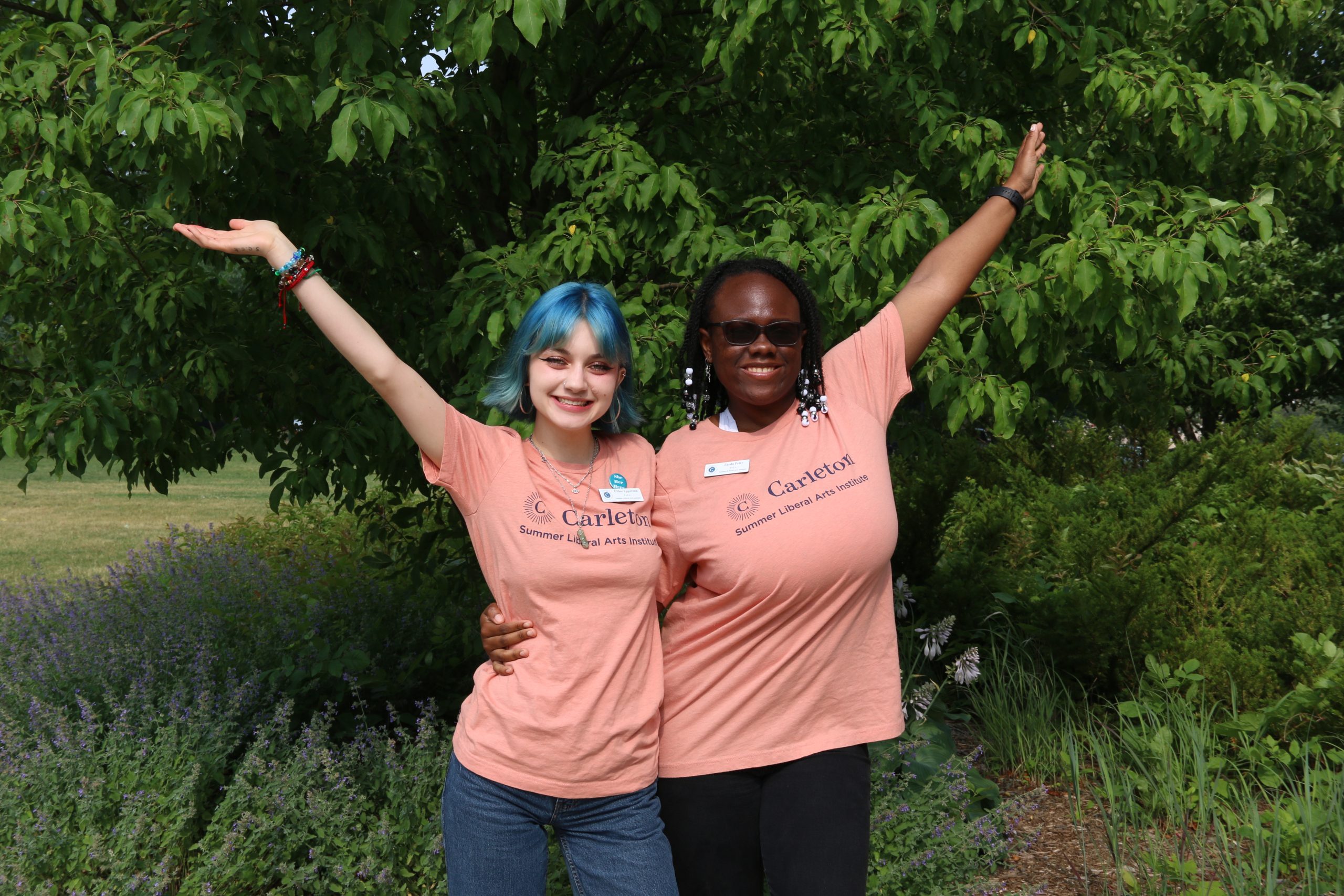 Two people wearing orange SLAC shirts smile and pose with their arms raised in the air.