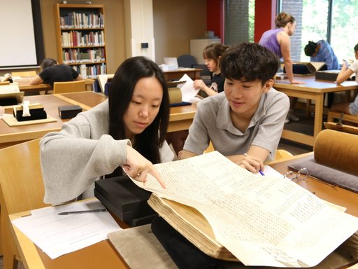 Two students studiously look over a primary text in library archives.