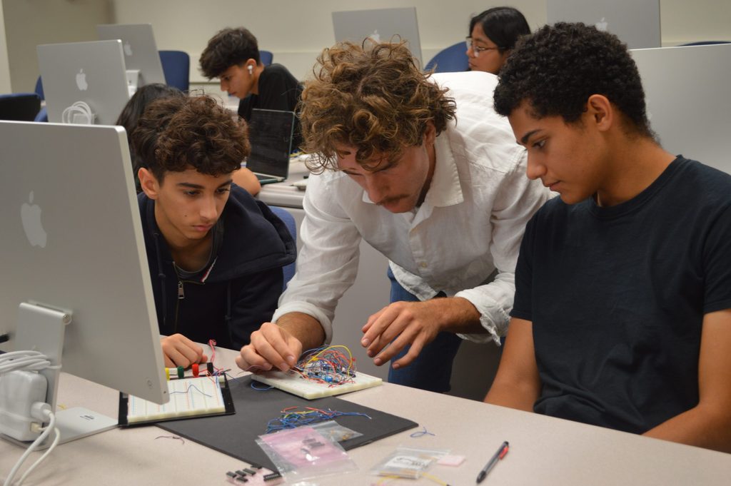 A teaching assistant helps two students build a computer component in a computer lab.
