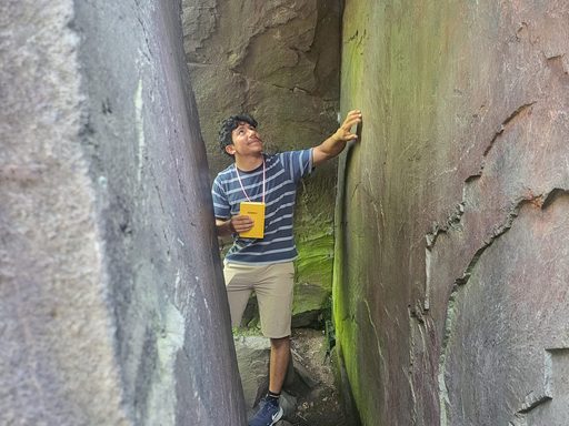 Student stands between two rock walls holding a field journal, and reaches up to touch one rock wall.