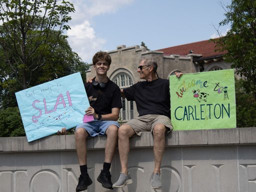 A student and parent sit on the Carleton College sign.